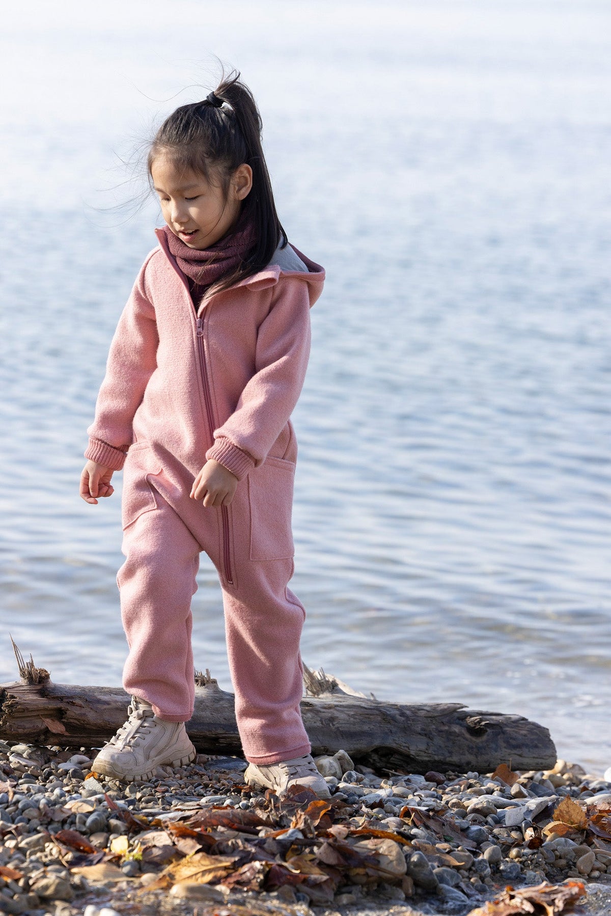 Child wearing a brown coat, blue hat, and pants on a white background