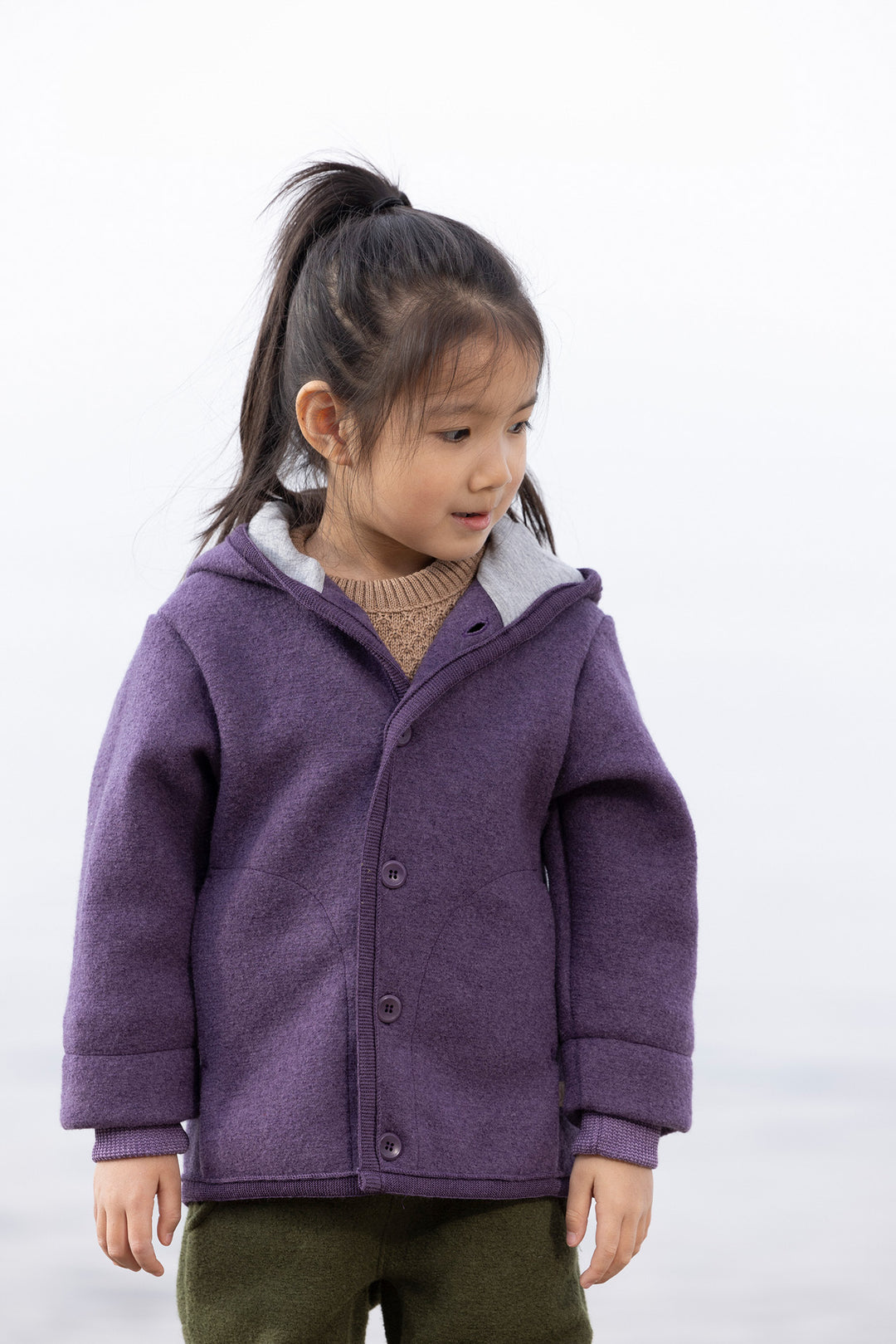 Child wearing a purple Disana boiled wool coat on a white background