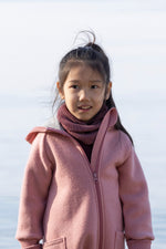 Young girl wearing a pink coat and a cassis coloured merino wool tube scarf from Disana against a light background