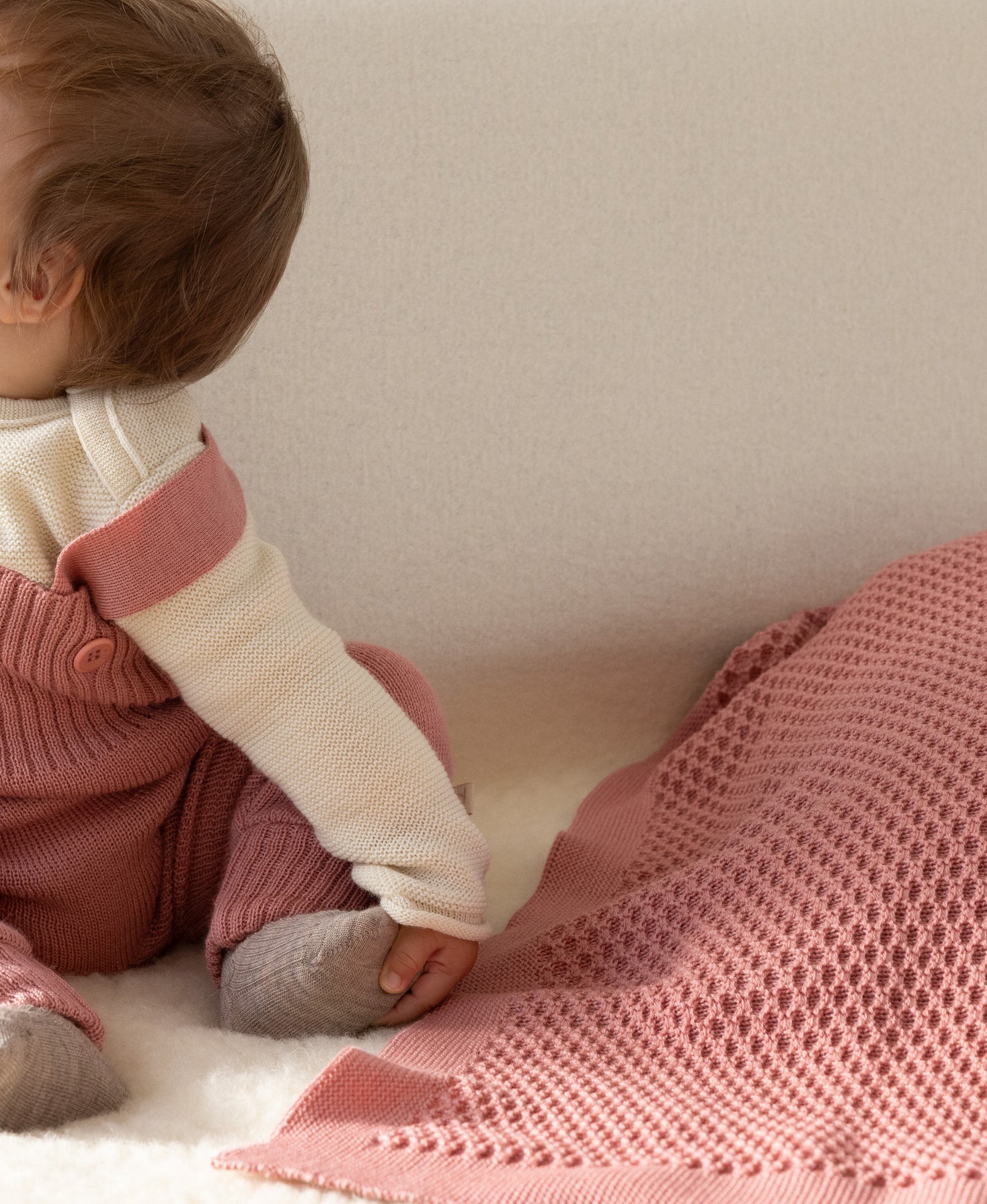 Baby sitting on a pink merino wool blanket with a neutral background