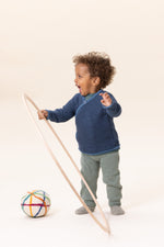 Child wearing blue Disana knit merino cardigan playing with a colorful ball and stick on a white background