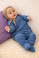 Baby wearing a blue knitted merino wool one-piece and brown bonnet on lambskin
