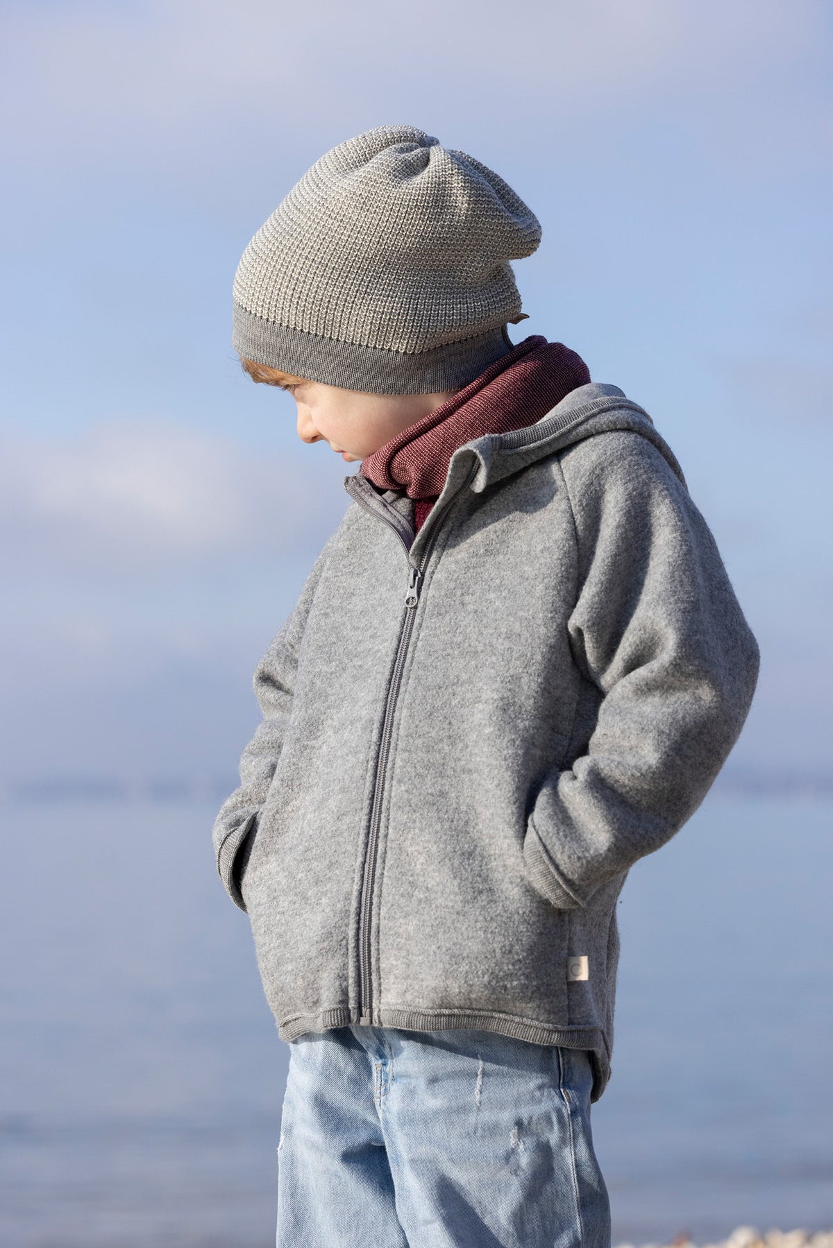 Child wearing a grey knit beanie and a boiled merino wool jacket in grey from Disana