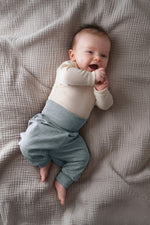 Baby wearing a cream top and light blue merino wool pants from Engel,  lying on a textured blanket
