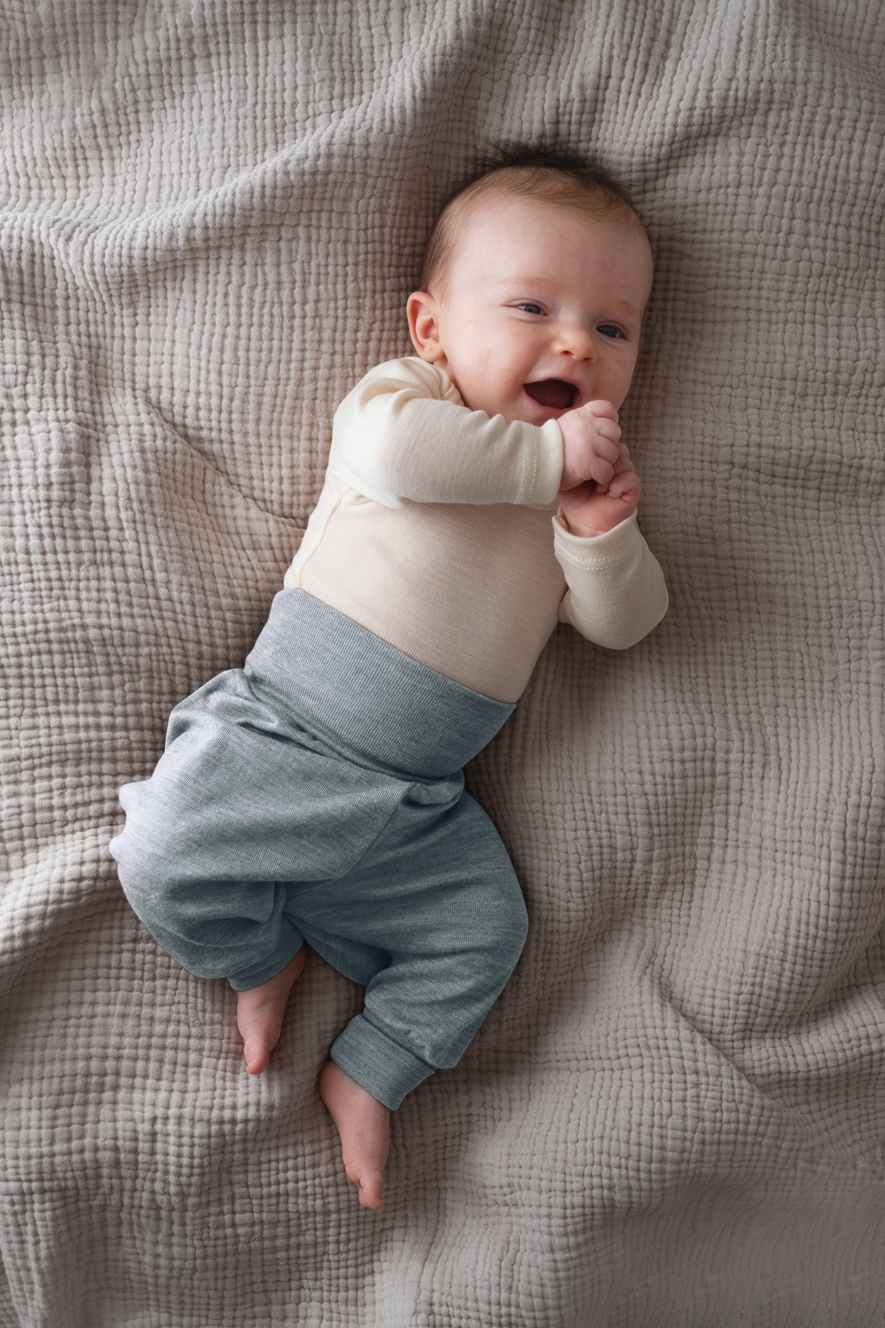 Baby wearing a cream top and light blue merino wool pants from Engel,  lying on a textured blanket