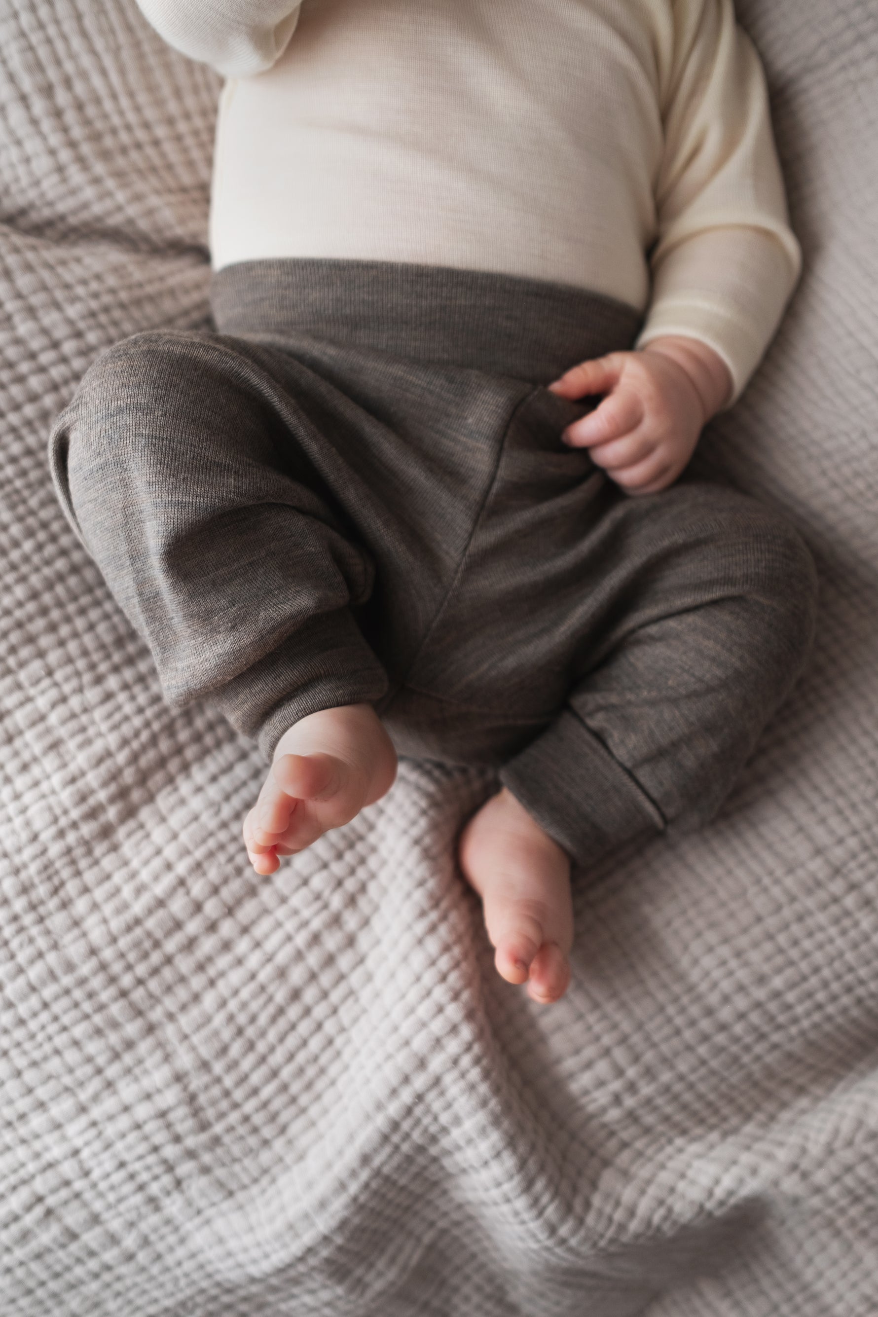 Baby wearing gray merino wool pants from Engel and a cream merino top on a textured beige blanket