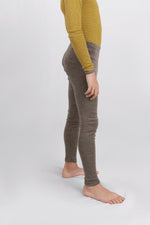 A side-profile view of a child wearing ribbed Engel merino leggings in a walnut color, paired with a yellow and gray striped long-sleeve top, standing barefoot against a light gray studio background.
