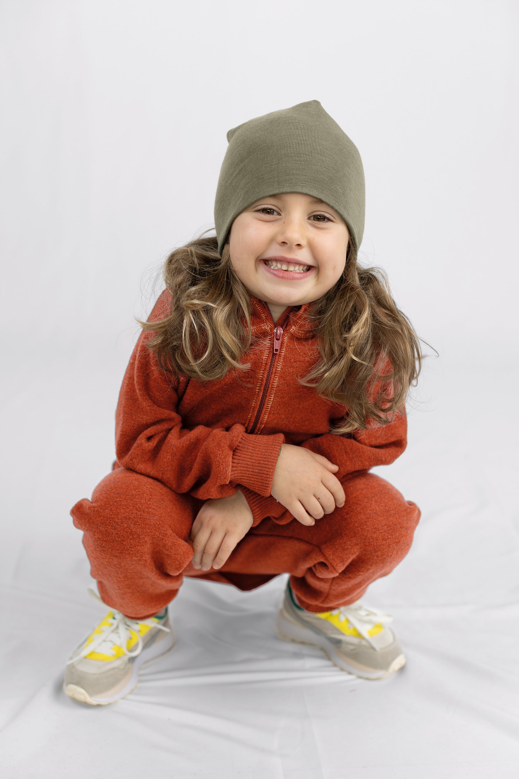 Child wearing a red outfit and olive Engel merino wool beanie on a white background