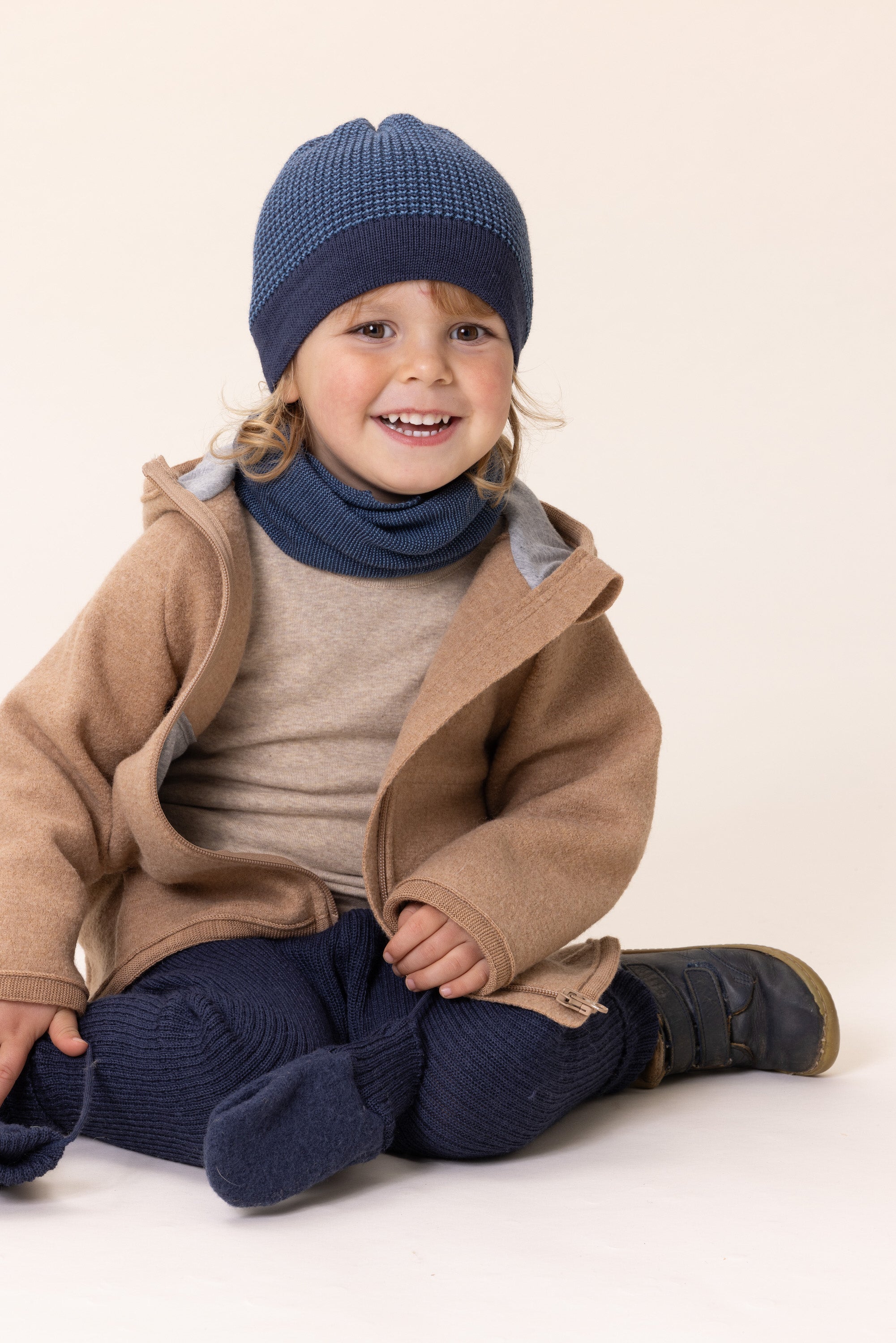 Child wearing a brown coat, blue hat, and pants on a white background